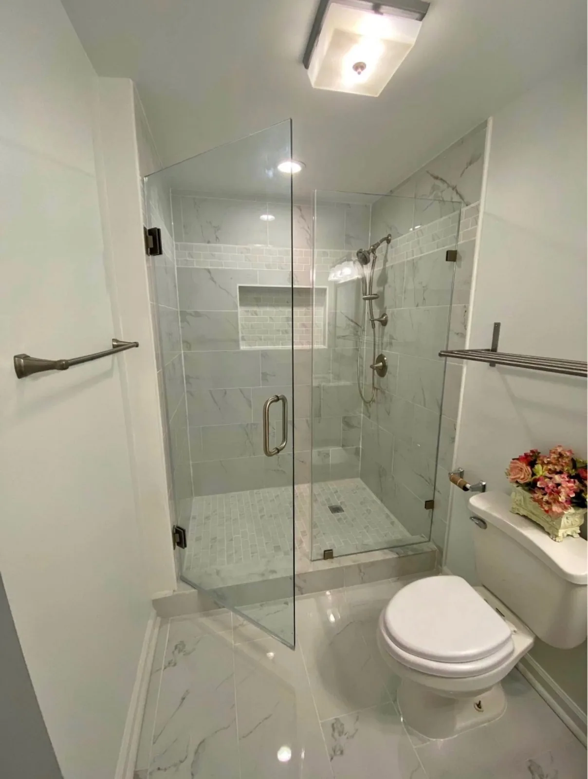 Corner shower with frameless glass, marble-look tile and a recessed niche in a compact bathroom