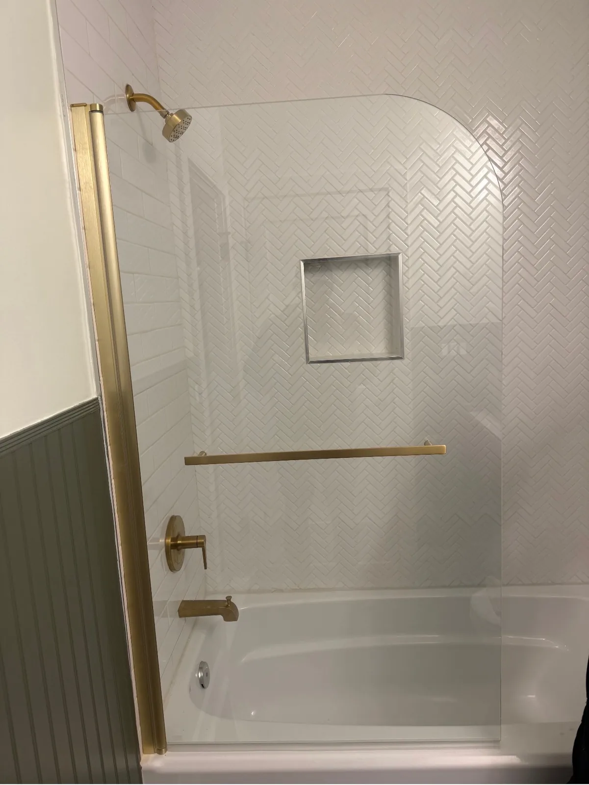 Tub and shower surround in white herringbone tile with brushed brass fixtures and a recessed niche