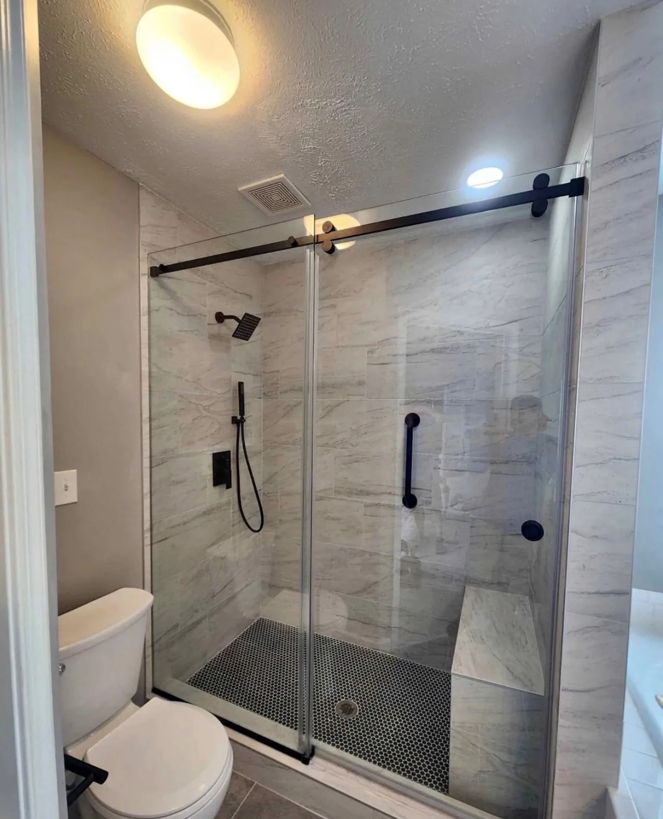 Walk-in shower with marbled grey tile, a sliding glass door, matte black fixtures and a penny-tile floor