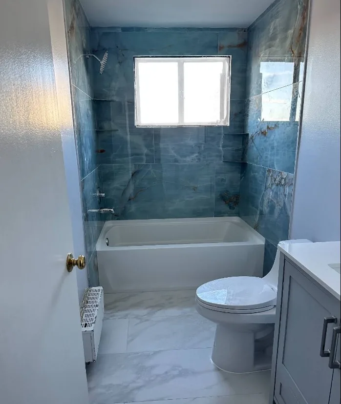 Compact bathroom with dramatic blue marbled tile, soaking tub-shower, and gray vanity