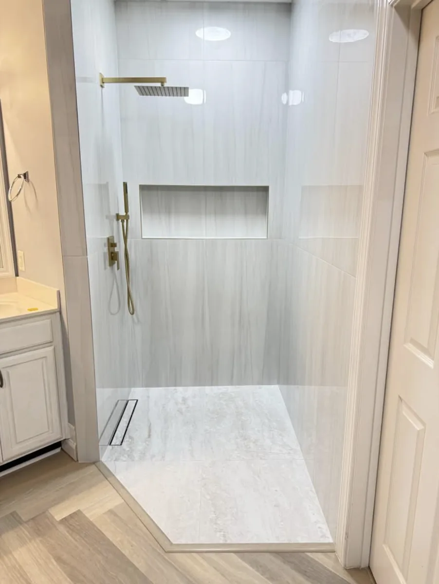 Walk-in shower with vertical vein-cut tile, brass fixtures, and a linear drain, built by DMV Home Improvement